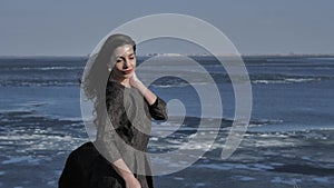 A young girl in a black dress strokes her hair,in the background ocean,sunny day