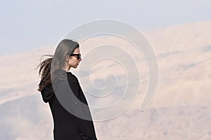 A young girl in a black sweatshirt and sunglasses on the background of rocks on the mountainside near the fortress of Al Karak in