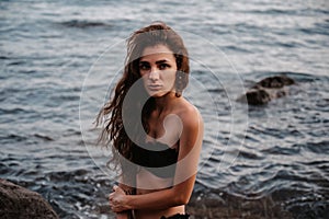 young girl in a black swimsuit is sitting sexy on rocks on the beach by the sea in summer