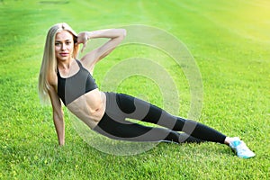 A young girl in a black tracksuit is stretching on the lawn. The concept of a healthy lifestyle. A copy of the space