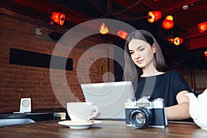 Young girl bloger freelancer photographer working on laptop in cafe