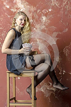 Young girl with blonde curly hair in a long dress with polka dots with playing cards
