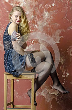 Young girl with blonde curly hair in a long dress with polka dots with playing cards