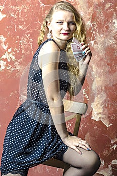 Young girl with blonde curly hair in a long dress with polka dots with playing cards