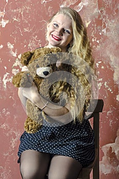 Young girl with blonde curly hair in a long dress with polka dots with teddy bear