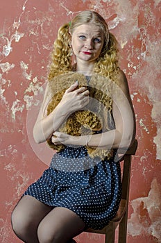 Young girl with blonde curly hair in a long dress with polka dots with teddy bear