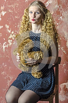 Young girl with blonde curly hair in a long dress with polka dots with teddy bear