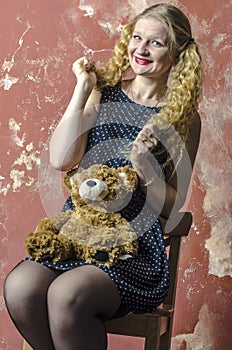 Young girl with blonde curly hair in a long dress with polka dots with teddy bear