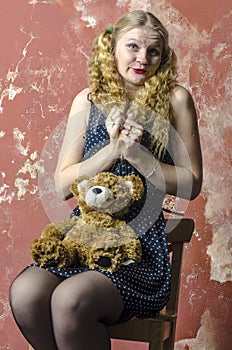 Young girl with blonde curly hair in a long dress with polka dots with teddy bear