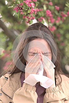 Young girl is blowing her nose near spring tree in bloom