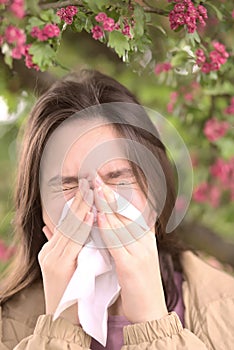 Young girl is blowing her nose near spring tree in bloom