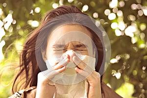 Young girl is blowing her nose near spring tree in bloom