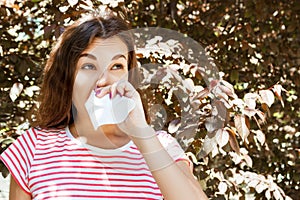 Young girl blowing her nose. Young girl with allergy in autumn park