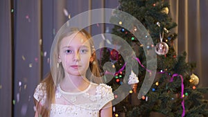 Young girl blowing up cracker on Christmas tree background in living room. Scared girl teenager exploding flapper on New