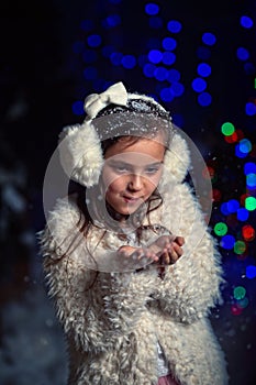 Young girl blows snowflakes in winter