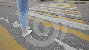 A young girl in blue jeans crosses a pedestrian crossing