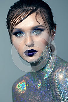 Young girl with blue professional make up and eyelash bundles, with body covered a lot of blue sparkles.