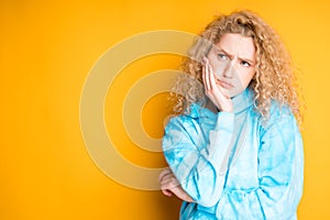 A young girl in a blue sweater stands against a bright background showing sadness. Emotions photo