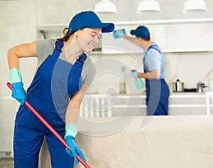 Young girl in blue uniform cleaning the floor in the kitchen