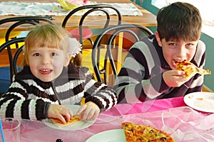 Young girl and boy eat delicious pizza with great pleasure in a children`s cafe