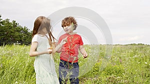 Young girl and boy looking flowers and plant at green meadow in village. Little sister and brother walking on