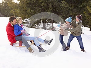 Young Girl And Boy Pulling Parents Through Snow On