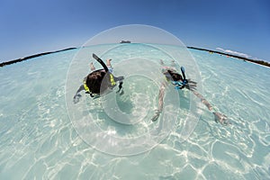 Young girl and boy snorkeling in crystal clear water with cruise ship in background with wide angle curved horizon.