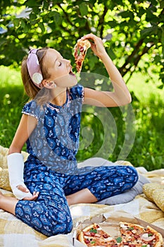 Young Girl With Broken Arm Enjoying Pizza in Sunlit Garden