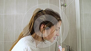 Young girl brushes her teeth with an irrigator in the bathroom side view