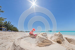 Young girl building sand castle on white beach with blue water and cruise ship in background. Beautiful sun flare overhead.