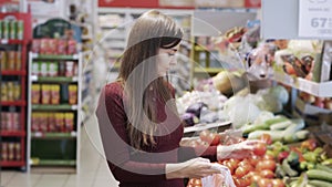 Young girl buys vegetables in grocery department of supermarket and puts them in plastic bag