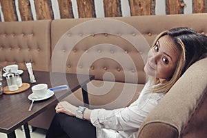 Young girl in cafe on sofa looks from behind shoulder, turning her head backwards