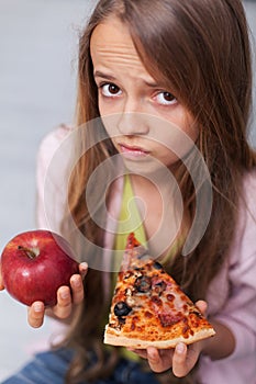 Young girl cannot decide between appetizing pizza and healthy apple photo