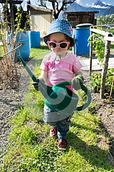 Young girl carrying a large green watering can as she helps in the vegetable garden