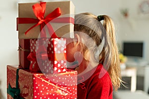 Young girl carrying stack of christmas presents. Happy kid at christmas time.