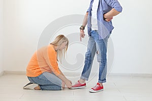 Young girl in casual clothes is sitting on her knees and touching the shoes of her domineering unidentified man posing photo
