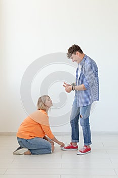 Young girl in casual clothes is sitting on her knees and touching the shoes of her domineering unidentified man posing photo