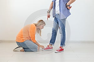 Young girl in casual clothes is sitting on her knees and touching the shoes of her domineering unidentified man posing