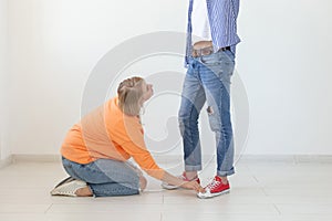 Young girl in casual clothes is sitting on her knees and touching the shoes of her domineering unidentified man posing