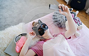 Young girl with cat mask on bed, taking selfie. Online dating concept.