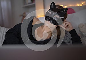 Young girl with cat mask and laptop indoors online dating and abuse concept.