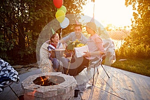 Young girl celebrating birthday with mother and father, recieving gifts sitting outdoors on a sunny summer day together