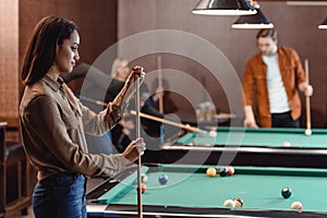 young girl chalking cue beside pool table at bar