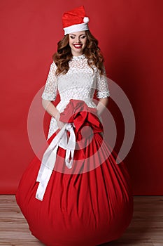 Young girl with charming smile, in Santa hat, with big bag with presents