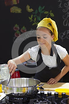 Young girl in a chef`s hat cooks in a large saucepan in a black