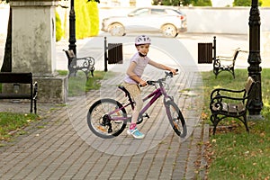 Young girl child with a safety helmet on sitting on her bike along a shaded path in the local public park with benches and