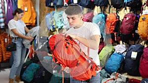 Young girl chooses and buys tourist backpack for summer hike in a sports equipment store