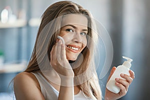 Young girl cleaning her face with tonic, removing makeup in front of mirror in bathroom