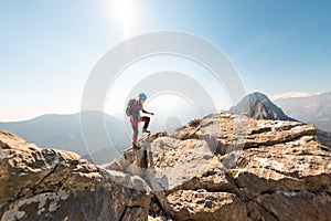 young girl climber in a helmet and with a backpack walks along a mountain range against the backdrop of mountains and climbing and