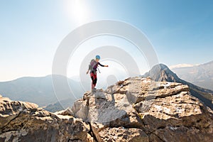 young girl climber in a helmet and with a backpack walks along a mountain range against the backdrop of mountains and climbing and